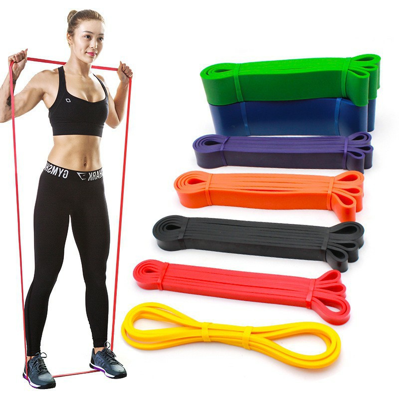 Người tập thể dục với dây kháng lực màu đỏ, bên cạnh là các dây kháng lực màu sắc khác nhau xếp chồng.