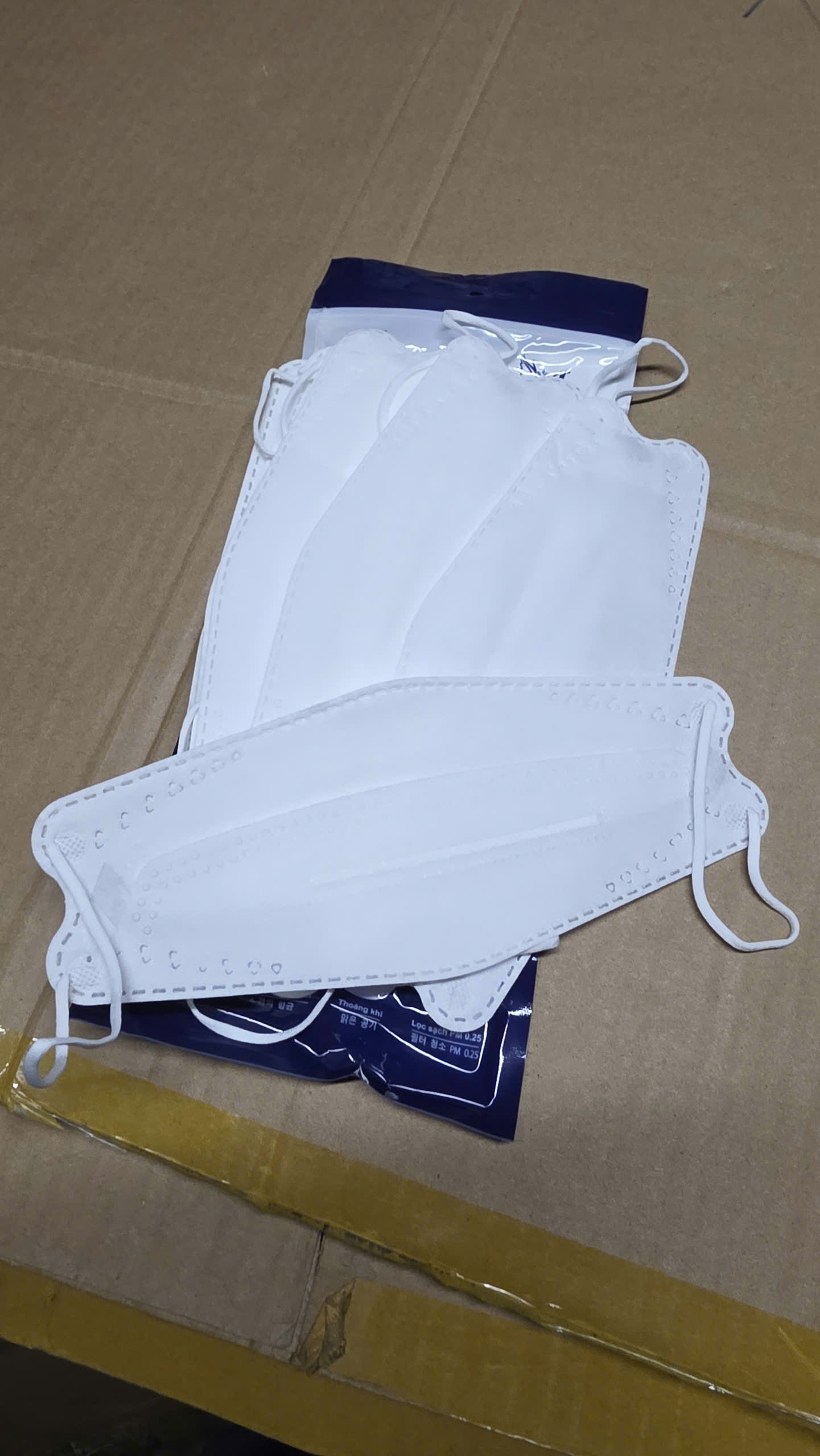Khẩu trang y tế không dệt vải trắng 3 lớp, đeo tai, đặt trên bìa carton.